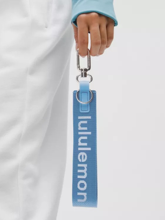 دستی با جاکلیدی بنددار آبی و نوشته سفید lululemon، کنار شلوار سفید
